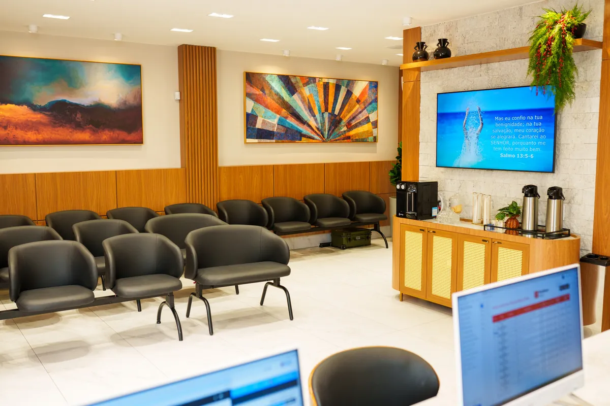 Sala de espera climatizada com televisão e painel de senhas